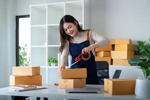 Woman use scotch tape to attach parcel box to prepare goods for the process of packaging, shipping, online sale internet marketing ecommerce concept startup business idea.