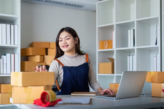 Startup SME small business entrepreneur SME or freelance Asian woman using a laptop with box, Young success Asian woman online marketing package box and delivery concept.