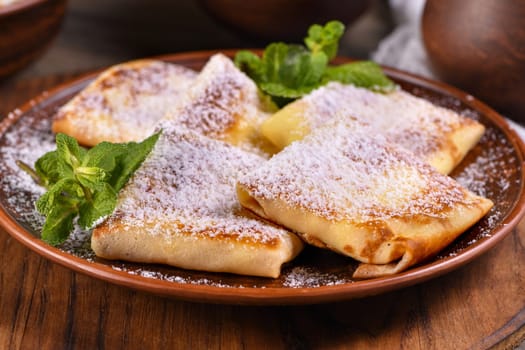 Thin pancakes filled with cottage cheese, honey and raisins, wrapped in an envelope, sprinkled with powdered sugar, garnished with mint. Festive dish for the pagan Slavic holiday Maslenitsa