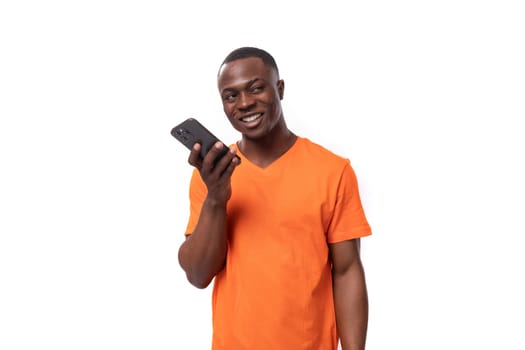 a young kind American guy with a short haircut dressed in an orange T-shirt speaks on the phone.