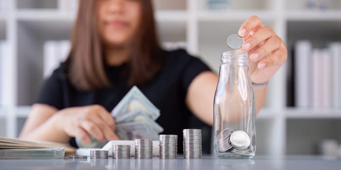 Woman saving money with hand putting coins in jug glass concept finance and accounting finance and saving money for future concept.
