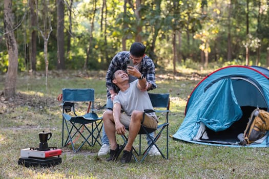 Asian LGBTQ couple tent in front of camp talking on smartphone in video chat or take a selfie.