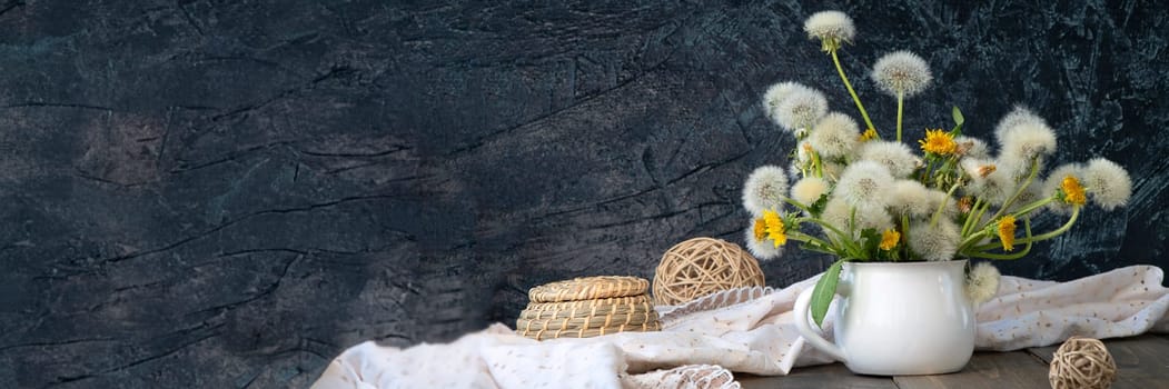 banner of air bouquet of dandelions in a white mug on a black textured background. soft focus