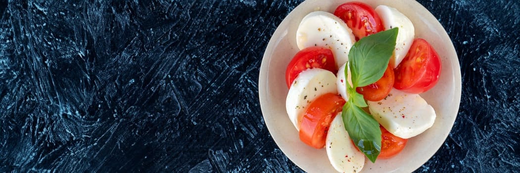 banner of caprese salad on a round plate. slices of juicy red tomato, with fresh mozzarella and basil leaves, poured with olive oil with spices. top view copy space