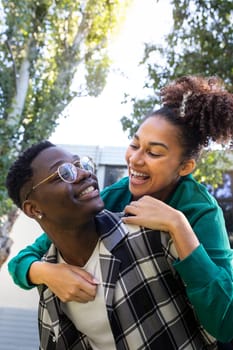 Vertical portrait of happy black man carrying girlfriend on the back. Playful, in love young couple. Boyfriend and girlfriend looking at each other eyes. Loving relationship.