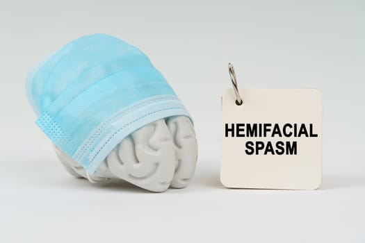 Medical concept. On a white surface next to the brain there is a notepad with the inscription - Hemifacial spasm