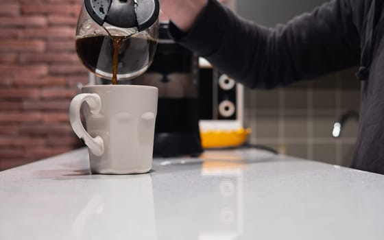 Man pouring coffee into cup at home, closeup. A hand pouring steaming coffee in to a cup