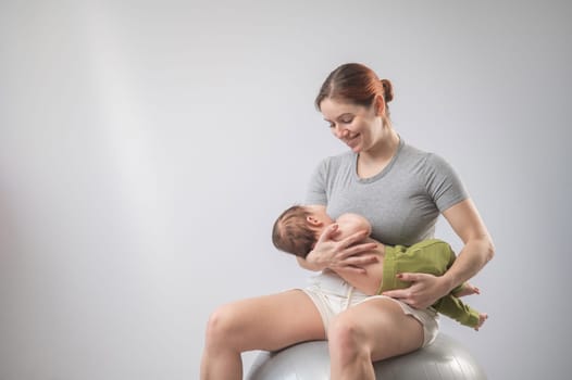 A Caucasian woman rocks her newborn son on a fitball. Copy space