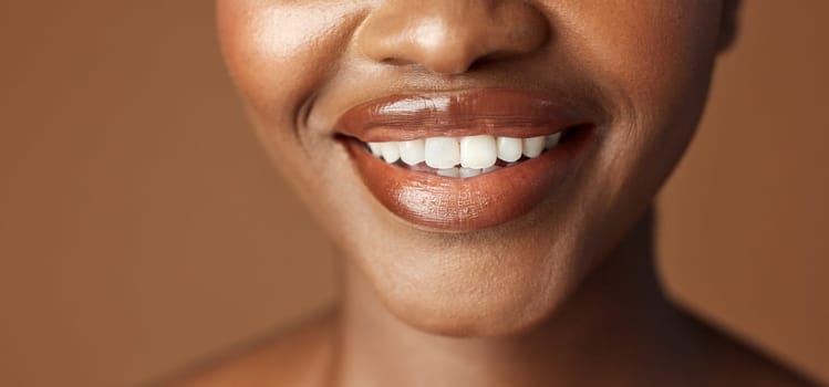 Closeup, lips and black woman with beauty, smile and skincare on a brown studio background. African person, girl and model with gloss, cosmetics and dermatology with clear skin, smooth and aesthetic.