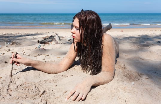 Youth, beauty, healthy lifestyle and nudity. Young fully naked woman with body covered with sand on the sea coast on a sunny day.