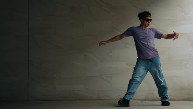 Skilled smart street dancer practice b-boy movement in building with gray background. Young handsome attractive choreographer perform energetic and active movement. Outdoor sport 2024. Sprightly.