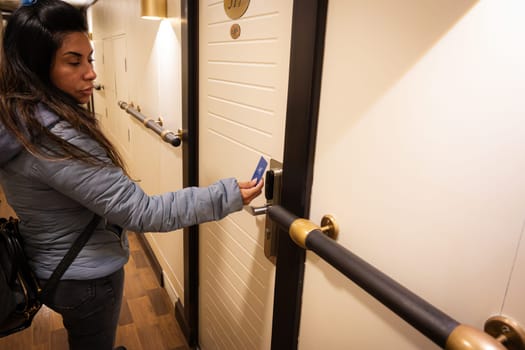 A latin woman is using a key card to unlock a hotel room door.