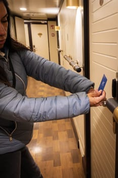 A latin woman in a corridor holding a key card to a door lock ,