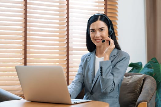 Female call center operator or customer service helpdesk staff working on workspace while talking on the headset to provide assistance for customer. Professional modern business service. Blithe