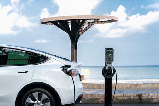 Electric car recharging battery at outdoor EV charging station for road trip or car traveling by the seascape, alternative and sustainable energy technology for eco-friendly car. Perpetual