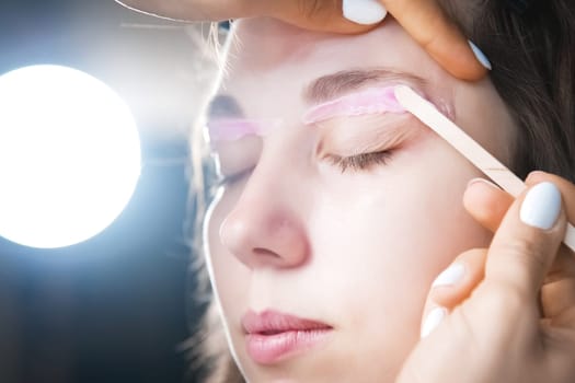 Hair removal, beauty and health concept. A young girl is getting an epilation procedure. A processional beauty worker is making depilation with hot wax.