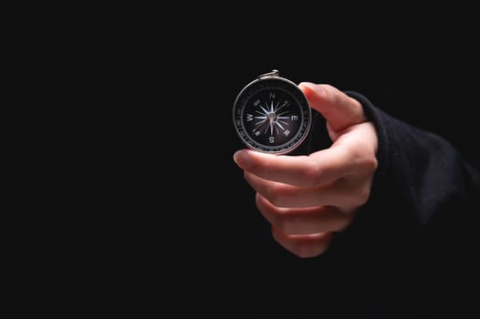 A woman's hand holds a compass showing south on a black background. A hand from the darkness holds out a compass, the concept of being lost and finding a solution or ideas with meanings