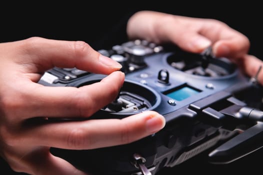 Remote control of FPV racing drone on black background in female hands, close-up.