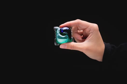 Cropped view of woman's hand holding laundry capsule on dark background, close-up.