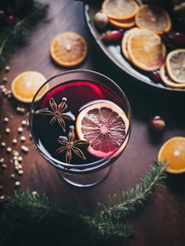 Glass of traditional mulled wine with orange and cranberry garnishes on a cozy Christmas table. The background is blurred with bokeh lights and candles, creating a warm and festive atmosphere