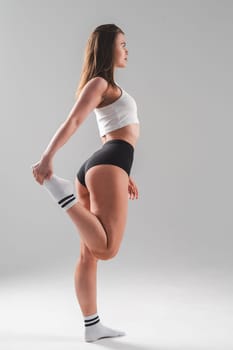Athletic Caucasian woman stretching her quadriceps on a white background. Vertical photo