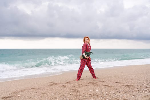 Sea Lady in plaid shirt with a christmas tree in her hands enjoys beach. Coastal area. Christmas, New Year holidays concep.