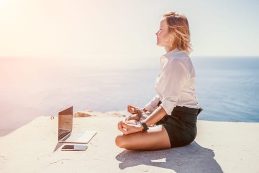 Happy girl doing yoga with laptop working at the beach. beautiful and calm business woman sitting with a laptop in a summer cafe in the lotus position meditating and relaxing. freelance girl remote work beach paradise