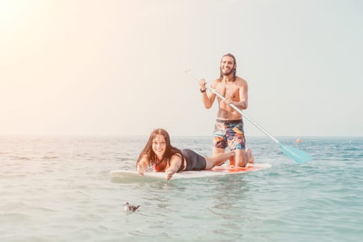 Sea woman and man on sup. Silhouette of happy young woman and man, surfing on SUP board, confident paddling through water surface. Idyllic sunset. Active lifestyle at sea or river