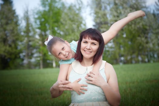 Happy mother and daughter enjoying rest, playing and fun on nature on a green lawn and with blooming apple tree in the background. Woman and girl resting outdoors in summer and spring day