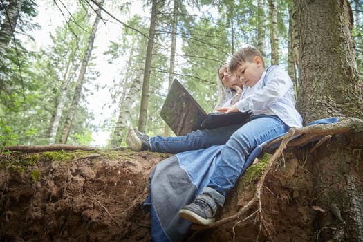 Mother and son with a laptops in the forest in summer. Fat young smart teenage boy and woman working with modern IT technologies in nature