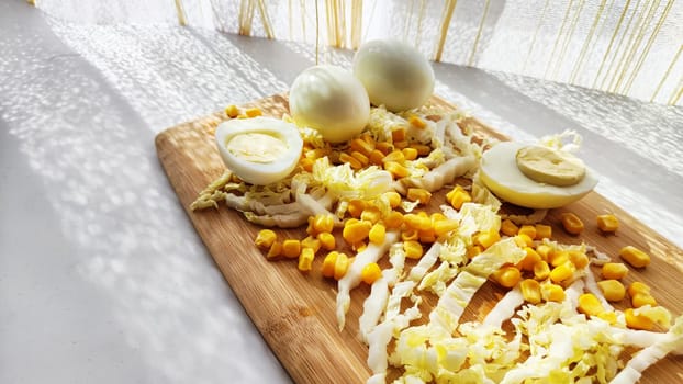 Chopped Peking cabbage, peeled eggs and yellow canned corn on cutting board as background. Cooking a healthy eco-friendly salad from natural products. Copy space and place for text