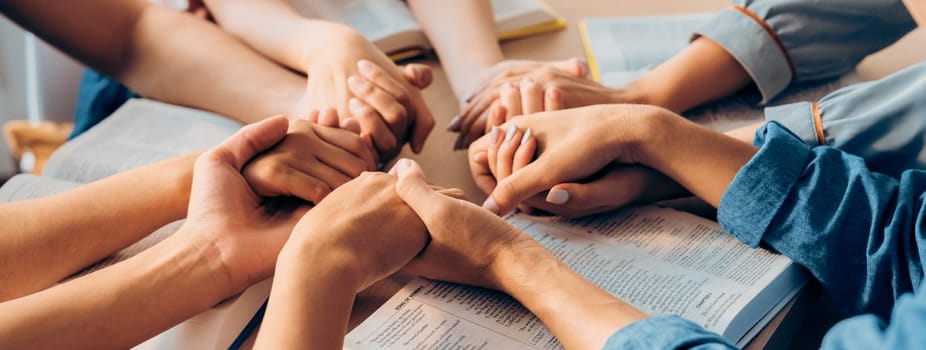 Cropped image of diversity people hand praying together at wooden church on bible book while hold hand together with believe. Concept of hope, religion, faith, god blessing concept. Burgeoning.