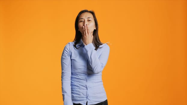 Flirty asian person blowing air kisses in studio, acting sweet with romantic gesture in front of camera. Young woman with casual clothes expressing love and sincere feelings.