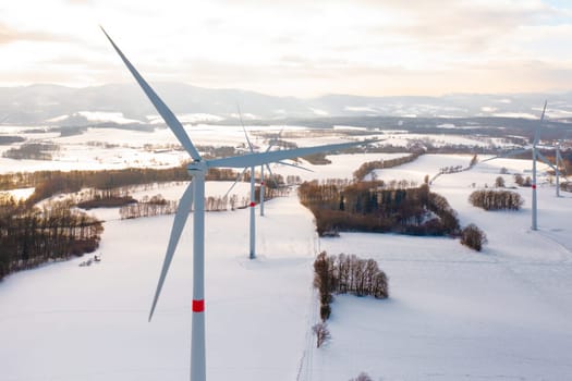 Amidst a frozen landscape with wind turbines, standing in the winter field at sunset.