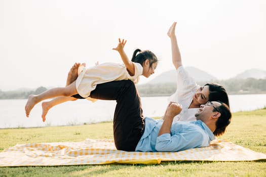 A family enjoys playful moments together. Father holds daughter high in air as she giggles and spreads her arms like wings, while mother watches with a smile outdoor. a precious moment of family fun