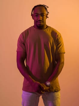 African American man with a modern and stylish haircut exudes confidence and charisma as he strikes a pose against an orange backdrop, showcasing a bold and vibrant expression of contemporary fashion and individuality.