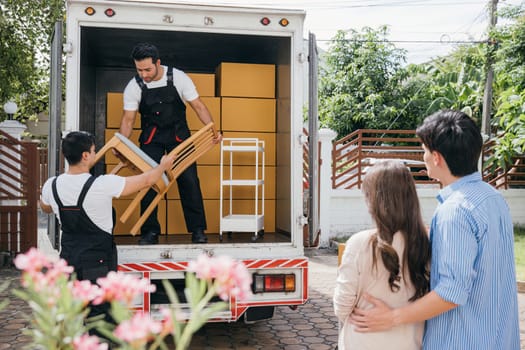 Moving house made easy for a couple with the help of a professional delivery team. They work together unloading and lifting cardboard boxes for efficient relocation. Moving Day Concept