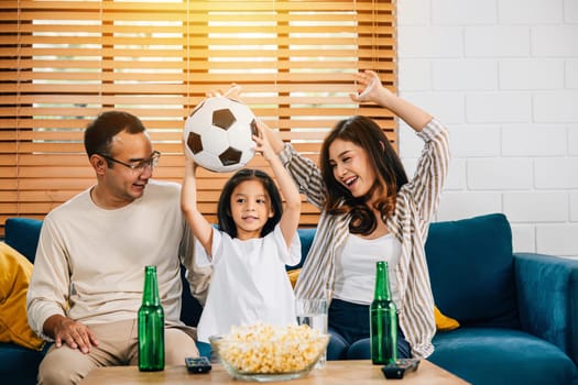 Excitement and togetherness abound as delighted parents and children celebrate a goal while watching a football match. With popcorn and a ball in hand, they share the joy of success at home.