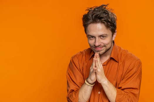 Sneaky cunning Caucasian young man with tricky face gesticulating and scheming evil plan, thinking over devious villain idea, cheats, jokes pranks. Guy isolated on orange studio background. Copy-space
