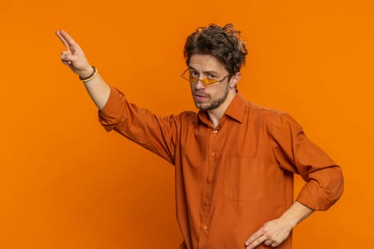 Stylish Caucasian man wearing yellow sunglasses listening music dancing disco fooling around having fun celebrating success victory winning good positive news. Happy guy isolated on orange background