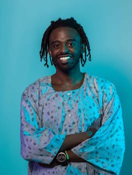 A Sudanese man adorned with modern dreadlocks stands proudly in traditional Sudanese attire, his arms crossed, conveying a blend of cultural heritage and contemporary style against a vibrant blue backdrop
