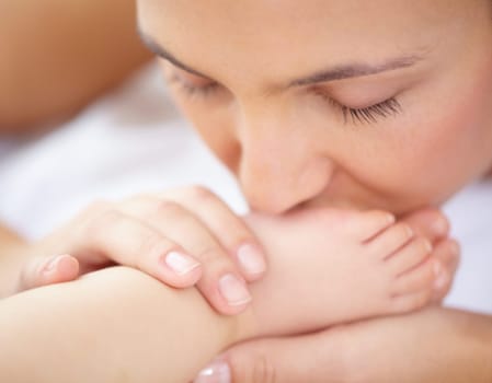 Mom, baby and kiss feet of child for love, care and relax in nursery room at home. Face, mother and closeup of foot of young kid for newborn development, healthy childhood growth or affection of bond.