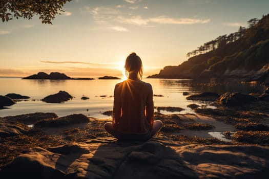 A girl meditates in a pose on the shore of the sea, lake in the rays of the sunset.