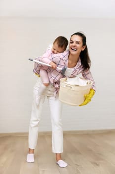 happy mother housewife is holding cute baby girl and basket with laundry and doing housework, Happy family having fun