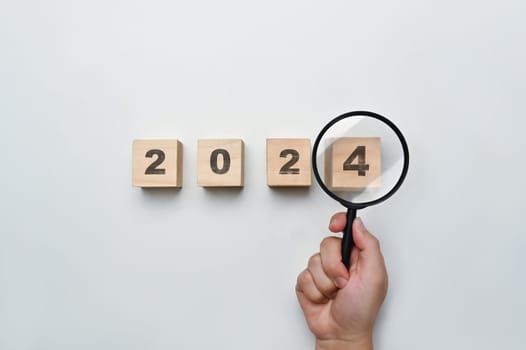 Magnifying glass and wooden cubes with 2024 year number on white background. New year goal and resolution concept.