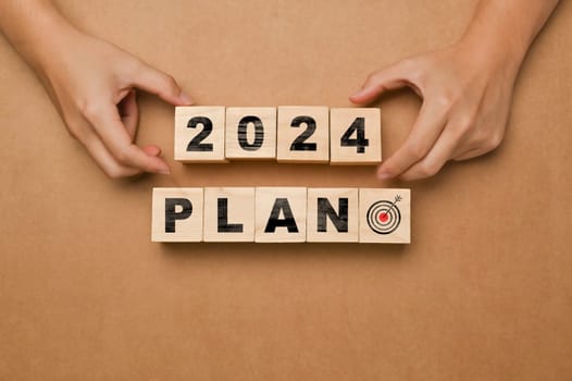 Hand place wooden cubes with 2024 PLAN on brown background. Business plan, goals and strategy concept.