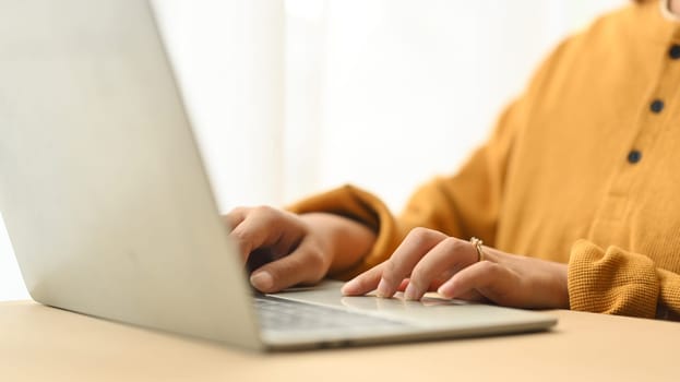 Cropped shot young woman wearing casual clothes working on laptop at home.