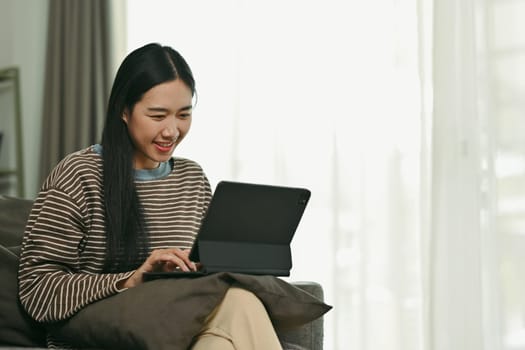 Beautiful Asian woman chatting on digital tablet browsing internet or working online at home.