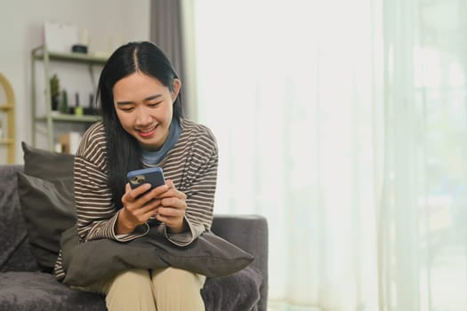 Cheerful young woman checking news and messaging in social network on mobile phone.