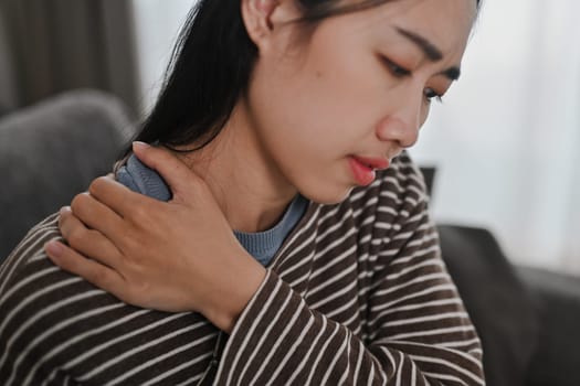 Upset young woman touching neck, suffering from pain and strain. Healthcare and problem concept.